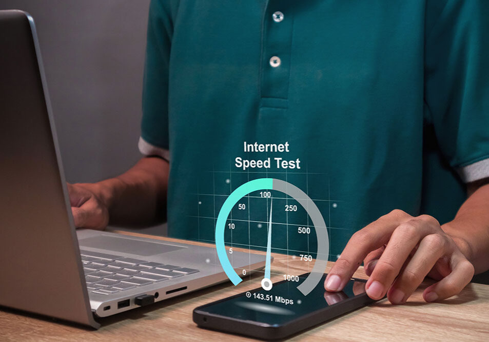 A person on a computer with a cell phone and a graphic that reads "Internet Speed Test".